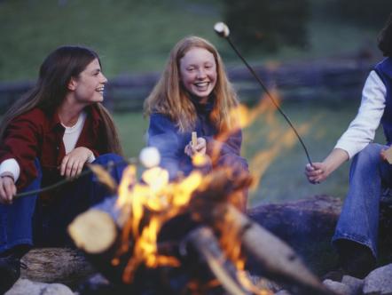 Three teenage girls in country field roasting marshmallows over campfire