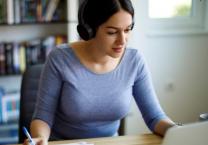 woman writing wearing headsphones